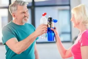 Older adults discussing hydration next to water bottles in a bright indoor setting, focused on fitness and health.