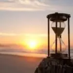 Hourglass on a sandy beach during sunset, with ocean waves softly lapping, representing Allore's Plumbing Services.