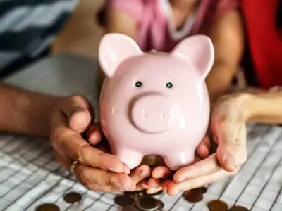 Pink piggy bank held by two people with coins on a table, symbolizing financial savings and investment for home improvements like tankless water heaters.