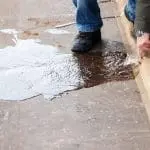 A foot and hand interacting with pooled water on pavement, showing plumbing maintenance by Allore's Plumbing Services.