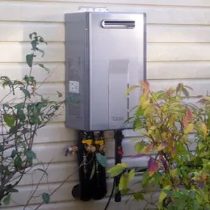 Tankless water heater mounted on a wall, surrounded by greenery, illustrating efficient home water heating solutions for stress reduction.