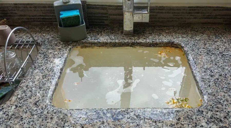Cluttered kitchen sink with debris-filled water, sponge holder, and dish rack, highlighting cleanliness issues.