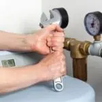 Hands with an adjustable wrench on a water heater pressure gauge by Allore's Plumbing Services LLC.