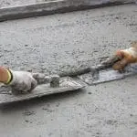 Workers smoothing fresh concrete with trowels, highlighting craftsmanship in plumbing services.