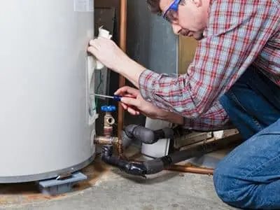 Man performing maintenance on a water heater, wearing safety goggles and using a screwdriver, highlighting the importance of regular water heater upkeep for efficient performance and safety.
