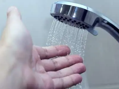 Hand testing water temperature from a chrome showerhead, illustrating issues with inconsistent water temperature in plumbing.