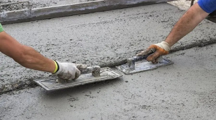 Two workers using trowels on freshly poured concrete, showcasing craftsmanship in plumbing services by Allore's Plumbing.