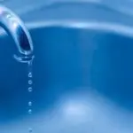 Blue water faucet dripping over a bathtub, showcasing plumbing services by Allore's Plumbing Services LLC in Stuart, FL.