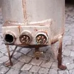 Rusty metal tank with connectors on cobblestone ground, illustrating plumbing maintenance for Allore's Plumbing Services LLC.