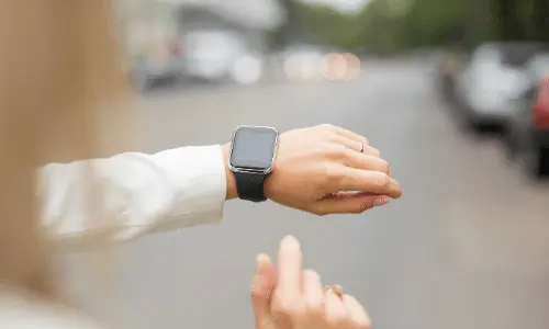 Person checking smartwatch while standing on a street, illustrating modern technology use and time management.