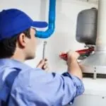 Plumber using a wrench on a water heater, representing Allore's Plumbing Services for effective holiday maintenance tips.