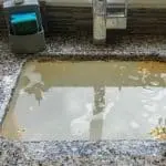 Waterlogged area with puddles and debris near utility fixtures, highlighting weather disruption for business context.