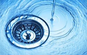 Water flowing into a stainless steel sink drain, illustrating plumbing elements relevant to water heater installation and maintenance.
