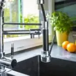 Modern chrome kitchen faucet with dark sink, potted plant, and oranges in bright light&mdash;Allore's Plumbing Services.