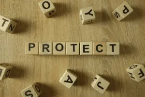 Wooden blocks spelling "PROTECT" surrounded by scattered letters, emphasizing the importance of safeguarding garbage disposals from improper waste.