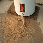 Water heater with a red valve, showing a water leak and soil accumulation, highlighting plumbing maintenance needs.