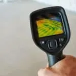 Thermal imaging camera held by hand, featuring a display screen and control buttons on a professional setting.