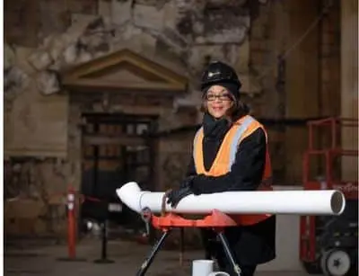Bennett, a Master Plumber and trailblazer in the skilled trades, posing with plumbing materials in a construction setting, showcasing resilience and dedication in the plumbing industry.
