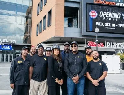 Group of diverse individuals, including Adrienne Bennett, posing outside Little Caesars Arena, celebrating community engagement and leadership in Detroit's plumbing industry.