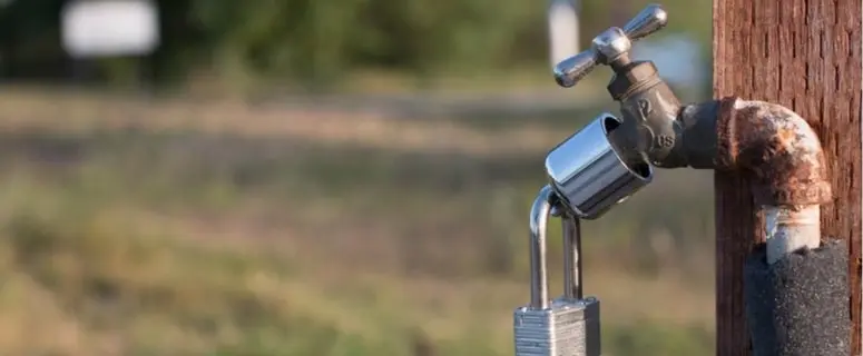 Outdoor plumbing faucet with a padlock, showcasing maintenance and security for seasonal water systems.