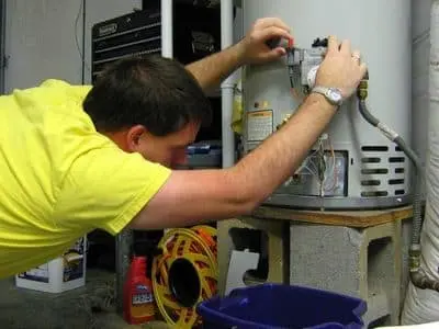 Person performing water heater maintenance by inspecting and adjusting components, emphasizing the importance of regular upkeep to prevent sediment buildup and ensure efficient performance.