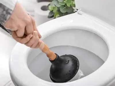 Person using a plunger in a toilet, demonstrating a common method to prevent clogged toilets, relevant to plumbing maintenance tips.
