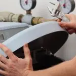 Hands using an adjustable wrench on plumbing machinery with pressure gauges, showcasing maintenance tools and techniques.