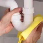 Person cleaning white plastic sink pipes with a yellow cloth, reflecting Allore's Plumbing maintenance tips for homeowners.