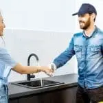 Two individuals shaking hands in a modern kitchen, discussing home improvement products, including a kitchen faucet.