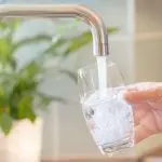 Modern faucet pouring water into a glass held by a hand, showcasing home plumbing services and hydration.