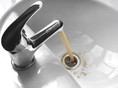 Faucet pouring discolored water into a sink, indicating potential issues with an aging water heater.