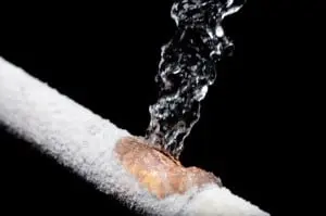 Frozen pipe bursting with water spraying out, highlighting the risk of plumbing damage and the importance of preventing pipe freezing.