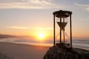 Hourglass on a wooden post at sunset, symbolizing the importance of timely well pump maintenance and plumbing care for homeowners.