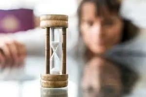 Hourglass symbolizing the importance of punctuality for plumbing services, with a woman in the background reflecting on time management.