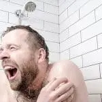 Joyful man showering in a tiled bathroom, enjoying a refreshing experience under a shower head.