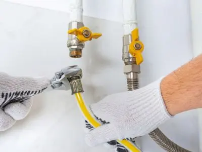 Plumber repairing gas line connections with adjustable wrench and yellow hose, emphasizing safety and professional maintenance.