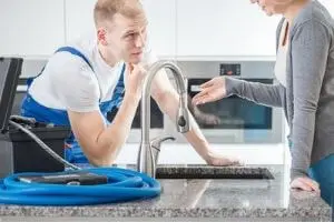Professional plumber discussing kitchen faucet repair with homeowner, highlighting the importance of expert plumbing services and addressing potential DIY mistakes.