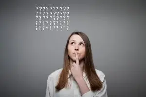 Woman pondering with finger on lips and question marks above her head, symbolizing confusion or uncertainty related to plumbing issues.