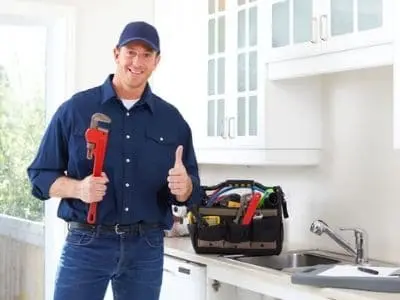 Professional plumber holding a wrench and giving a thumbs-up, standing in a kitchen with a toolbox, representing plumbing repair services and expertise in addressing issues like slab leaks.
