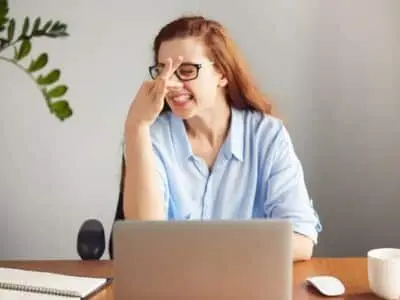 Woman showing frustration while working on a laptop, representing challenges faced with plumbing issues like garbage disposal odors and clogs.