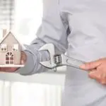 Person holding a house model and an adjustable wrench, representing home improvement for Allore's Plumbing Services LLC.