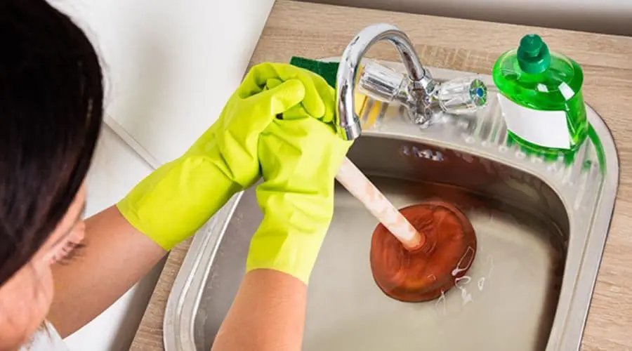 Person using a plunger in a clean sink with bright green gloves, showcasing practical home maintenance solutions.