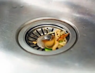 Food scraps and organic waste in a kitchen sink drain, highlighting the importance of keeping foreign objects out to prevent plumbing clogs during summer cookouts.
