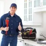 Smiling plumber in a blue shirt gives thumbs up in a well-lit kitchen, representing Allore's Plumbing Services LLC.