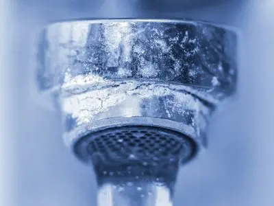 Close-up of a faucet aerator showing mineral scale buildup, indicating signs of hard water issues, relevant to water filtration and softener discussions.