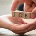 Two hands hold a wooden block labeled "JOB," representing employment opportunities connected to Allore's Plumbing Services.