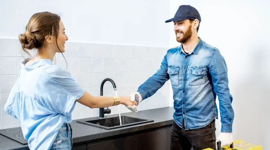 Man in blue cap and woman in casual top shaking hands in a bright kitchen with delivery packages. Home service interaction.