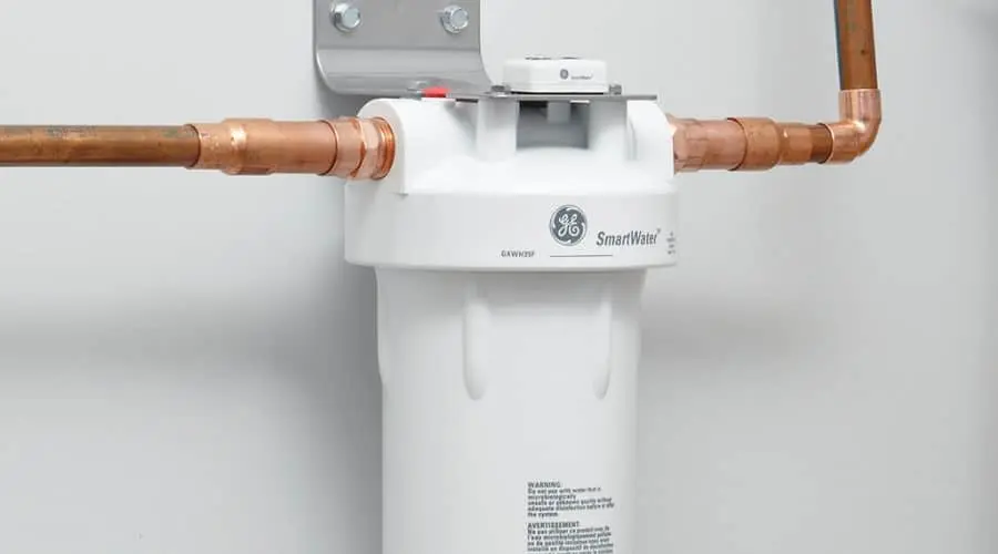Water filtration system with white housing and copper pipes, featuring compliance labels by Allore's Plumbing Services LLC.