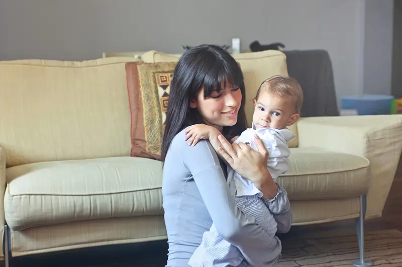 Mother holding baby in a cozy living room, showcasing warmth and family connection.