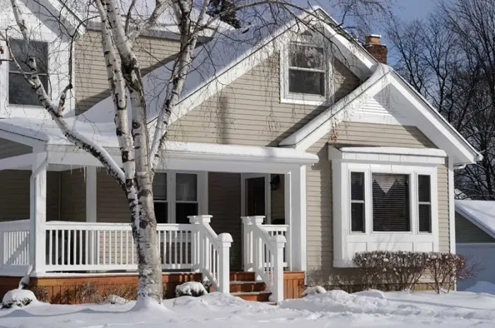 House with snow-covered porch and birch trees, representing winter heating needs for residential plumbing and HVAC services.